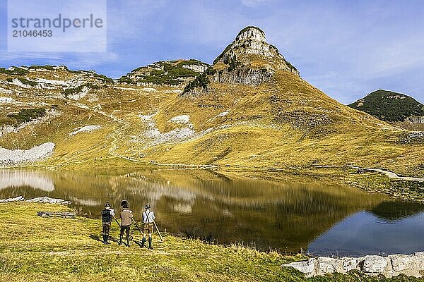 Drei Männer spielen Alphorn am Augstsee auf dem Berg Loser. Das österreichische Alphornbläser-Trio Klangholz. Im Hintergrund der Berg Atterkogel. Herbst  gutes Wetter  blauer Himmel. Spiegelung. Altaussee  Bad Aussee  Ausseer Land  Totes Gebirge  Steiermark  Oberösterreich  Österreich  Europa