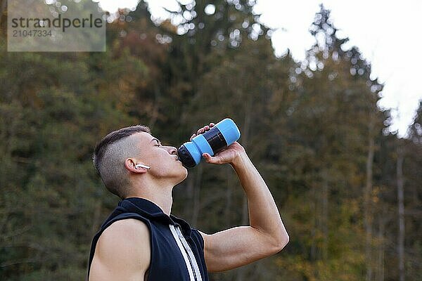 Junger Mann trinkt beim morgendlichen Joggen im Freien Wasser aus einer Flasche