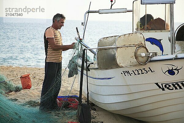 Fischer in Armacao de Pera  Algarve  Portugal  Fischer  der am Strand ein Netz neben einem Boot vorbereitet. Im Hintergrund das Meer und helles Sonnenlicht  Europa