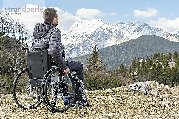 Foto eines jungen behinderten Mannes im Rollstuhl  der draußen in der Natur Berge und Natur beobachtet