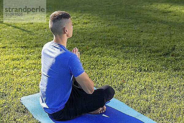 Junger Mann in Sportkleidung sitzt im Park und macht Yoga