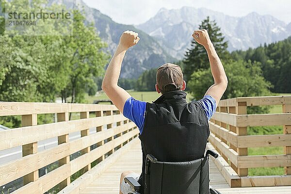 Behinderter junger Mann im Rollstuhl in der Natur  aufgeregt und voller Optimismus wie ein Gewinner