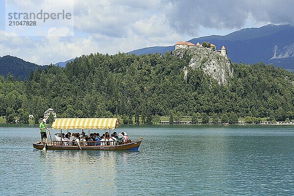 SLOWENIEN  BLED  15. JULI 2019: Traditionelles Touristenboot. Schöner Bergsee im Sommer mit Burg auf Felsen und Alpen im Hintergrund