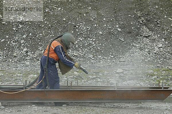 Mann beim Sandstrahlen eines I Trägers als Vorbereitung für den Anstrich