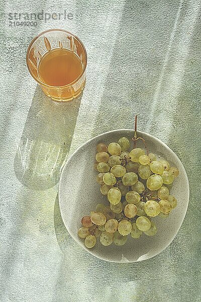 Ein Zweig weißer Trauben  auf einem grauen Teller  mit einem Glas Weißwein  Draufsicht  natürliches Licht  Lebensmittelkonzept  keine Menschen