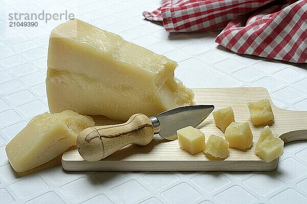 Ein Stück Parmesankäse und zerteilte Käsestückchen auf Holzbrett