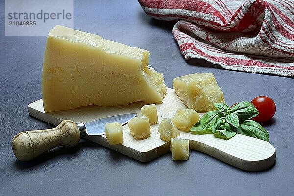 Ein Stück Parmesankäse und zerteilte Käsestückchen auf Holzbrett