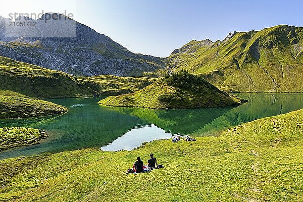 Menschen sitzen auf einer Wiese am Schrecksee und genießen ein Picknick vor einer malerischen Berg- und Seenlandschaft  Allgäuer Alpen  Bad Hindelang  Allgäu  Bayern  Deutschland  Europa