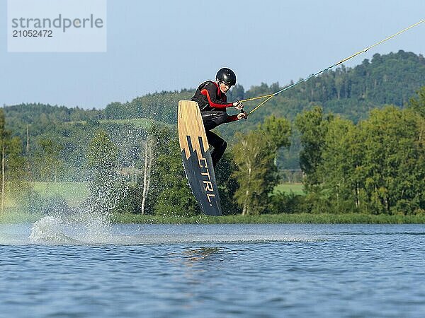 Junger Mann bei Sprung mit Wakeboard im See  Wassersport  Wasserski im Wakepark  Stráž pod Ralskem  Tschechin