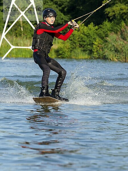 Junger Mann bei sportlicher Fahrt mit Wakeboard im See  Wassersport  Wasserski im Wakepark  Stráž pod Ralskem  Tschechin