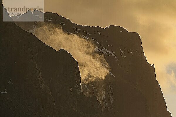 Die Gischt eines Wasserfalls sprüht nach oben  starker Wind  Berge  Morgenlicht  Gegenlicht  Ostisland  Island  Europa