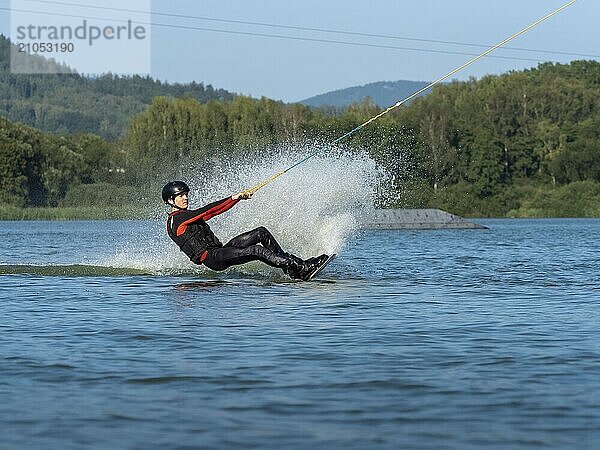 Junger Mann bei sportlicher Fahrt mit Wakeboard im See  Wassersport  Wasserski im Wakepark  Stráž pod Ralskem  Tschechin