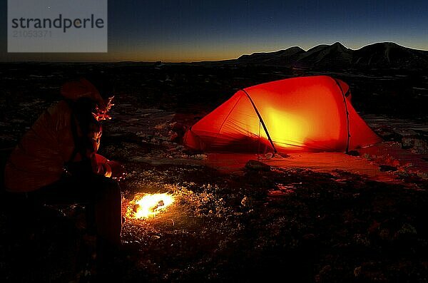 Mann mit Lagerfeuer und erleuchtetem Zelt  Engerdalsfjellet  im Hintergrund der Gipfel Rendalssölen  Hedmark Fylke  Norwegen  Norwegen  Europa