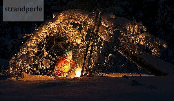 Mann grillt Wurst am Lagerfeuer unter einer verschneiten Kiefer  Gällivare  Norrbotten  Lappland  Schweden  Lappland  Schweden  Europa