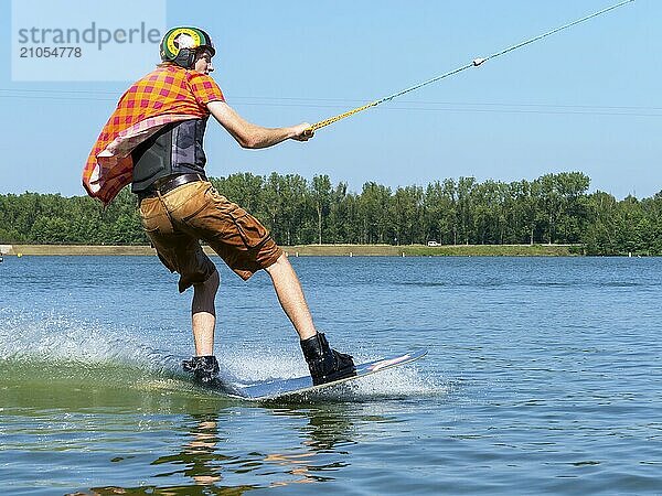 Junger lässiger Mann mit flatternden Hemd auf Wakeboard im See  Wasserski und Wakepark  Stráž pod Ralskem  Tschechin