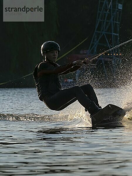 Junger Mann mit Wakeboard im See  rasante Fahrt  Wassersport  Wasserski im Wakepark