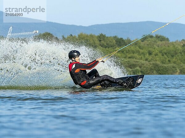 Junger Mann bei sportlicher Fahrt mit Wakeboard im See  Wassersport  Wasserski im Wakepark  Stráž pod Ralskem  Tschechin