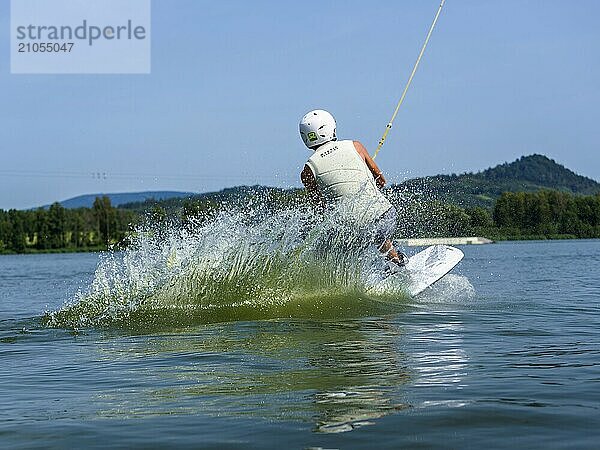 Junger Mann bei Sprung mit Wakeboard in den See  Wassersport  Wasserski im Wakepark  Stráž pod Ralskem  Tschechin