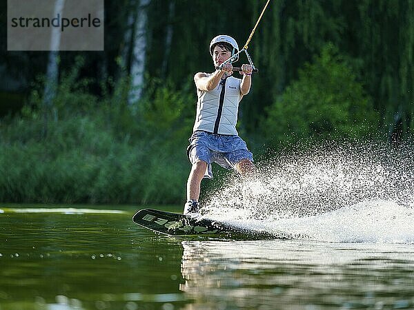 Sportlicher junger Mann mit Helm und Weste auf Wakeboard im See  Wassersport  Wasserski im Wakepark