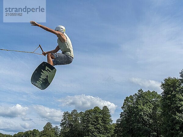 Junger Mann bei Sprung und Flug mit Wakeboard  Wassersport und Wasserski im Wakepark