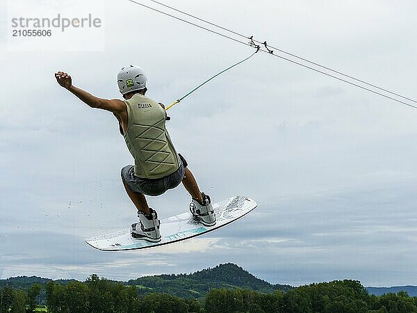 Junger Mann bei Sprung mit Wakeboard über den See  Wassersport  Wasserski im Wakepark  Stráž pod Ralskem  Tschechin