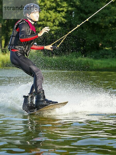 Junger Mann bei sportlicher Fahrt mit Wakeboard im See  Wassersport  Wasserski im Wakepark  Stráž pod Ralskem  Tschechin