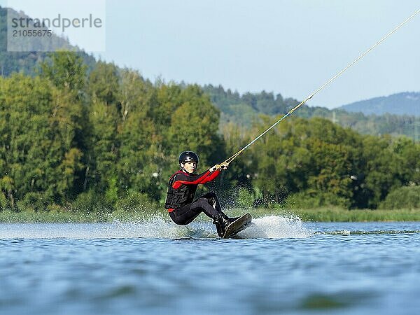 Junger Mann bei sportlicher Fahrt mit Wakeboard im See  Wassersport  Wasserski im Wakepark  Stráž pod Ralskem  Tschechin