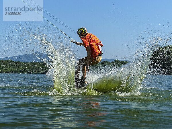 Junger lässiger Mann mit flatternden Hemd auf Wakeboard bei Sprung in den See  Wasserski und Wakepark  Stráž pod Ralskem  Tschechin