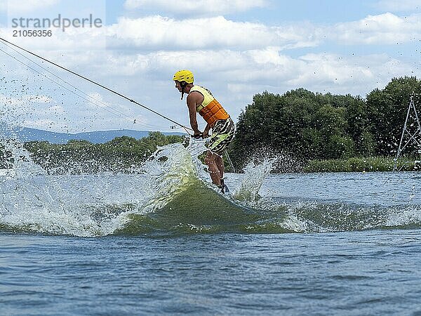 Sportlicher Mann bei Sprung mit Wakeboard  Wassersport  Wasserski und Wakepark