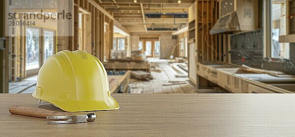 Gelber Schutzhelm und Hammer auf einem Holzhintergrund mit Hausrenovierung auf der Baustelle im Hintergrund