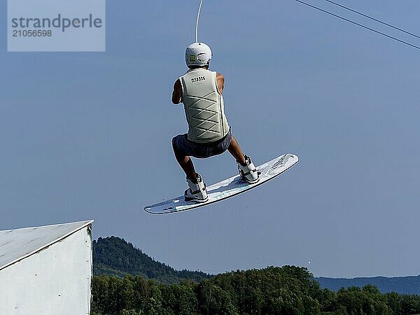 Junger Mann bei Sprung mit Wakeboard über Schanze und Hindernis  Wassersport  Wasserski im Wakepark  Stráž pod Ralskem  Tschechin