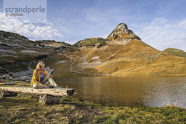 Augstsee und der Berg Atterkogel auf dem Loser. Eine Wanderin sitzt auf einer Bank und liest ein Buch. Herbst  gutes Wetter  blauer Himmel. Altaussee  Bad Aussee  Ausseer Land  Totes Gebirge  Steiermark  Oberösterreich  Österreich  Europa