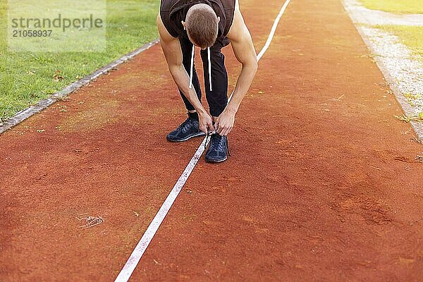 Junger Mann bindet Schuhe und bereitet sich auf das morgendliche Joggen im Freien auf der Laufstrecke vor