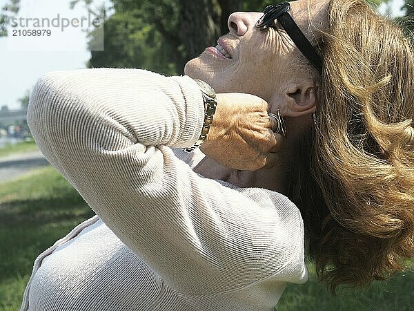 Eine ältere Frau genießt friedlich einen sonnigen Tag im Park  die Augen geschlossen  sich im warmen Sonnenlicht sonnend  Zufriedenheit und Entspannung ausstrahlend