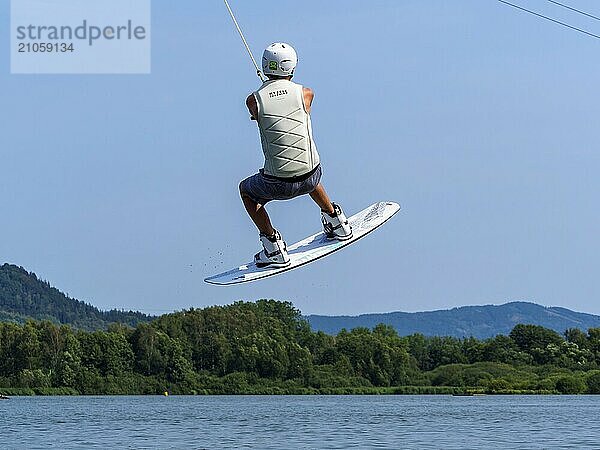 Junger Mann bei Sprung mit Wakeboard über Schanze und Hindernis  Wassersport  Wasserski im Wakepark  Stráž pod Ralskem  Tschechin