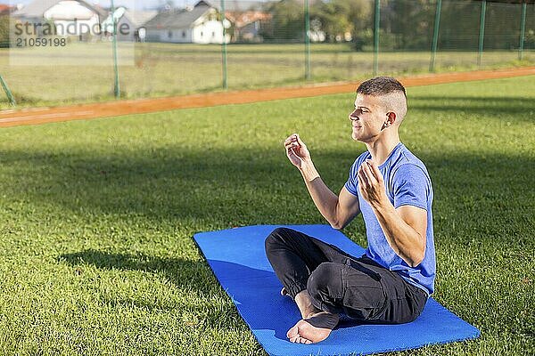 Junger Mann in Sportkleidung sitzt im Park und macht Yoga