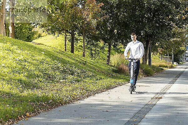 Fröhlicher und lässiger Mann fährt Elektroroller im Stadtpark