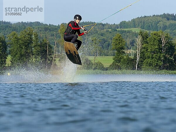 Junger Mann bei Sprung mit Wakeboard im See  Wassersport  Wasserski im Wakepark  Stráž pod Ralskem  Tschechin