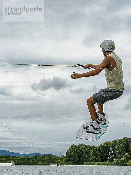 Junger Mann bei Sprung mit Wakeboard  Wassersport  Wasserski im Wakepark