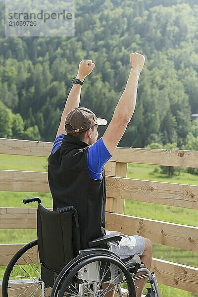 Behinderter junger Mann im Rollstuhl in der Natur  aufgeregt und voller Optimismus wie ein Gewinner