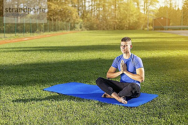 Junger Mann in Sportkleidung sitzt im Park und macht Yoga