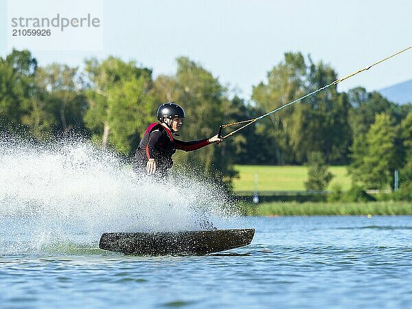 Junger Mann bei sportlicher Fahrt mit Wakeboard im See  Wassersport  Wasserski im Wakepark  Stráž pod Ralskem  Tschechin