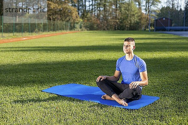 Junger Mann in Sportkleidung sitzt im Park und macht Yoga