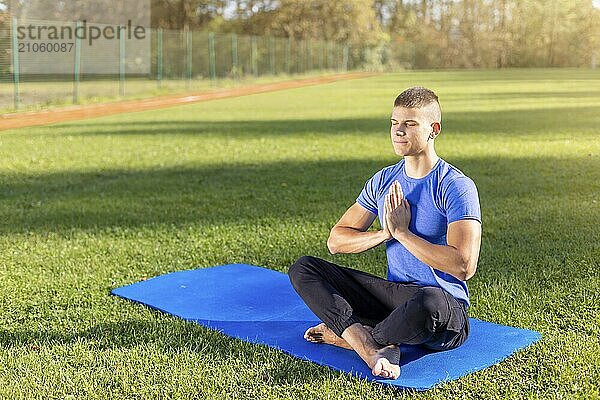 Junger Mann in Sportkleidung sitzt im Park und macht Yoga