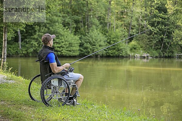 Fröhlicher und junger behinderter Mann beim Angeln an einem See in der Natur. Beliebter Sport für Querschnittsgelähmte