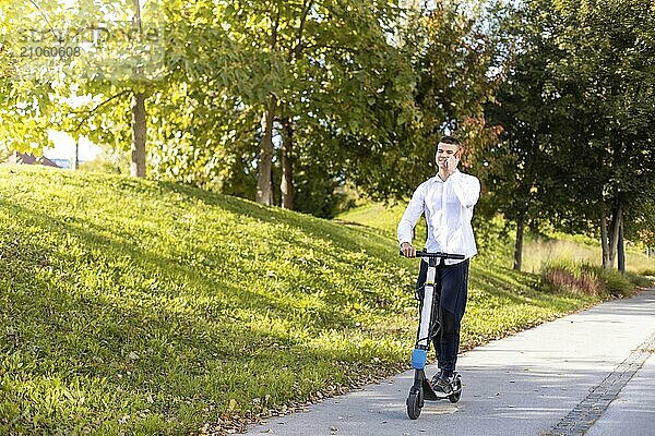 Fröhlicher und lässiger Mann fährt Elektroroller im Stadtpark und spricht am Telefon