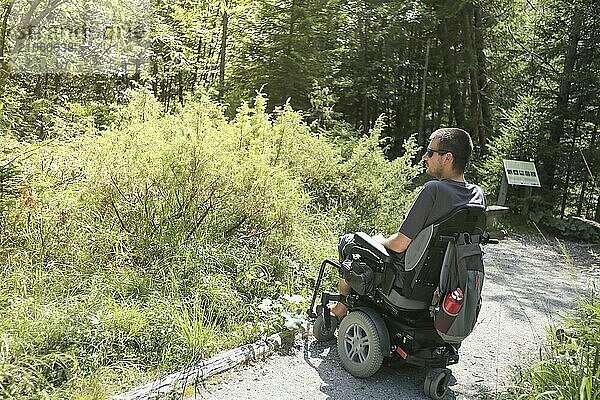 Glücklicher Mann im Rollstuhl in der Natur. Erkundung der Waldwildnis auf einem zugänglichen Feldweg