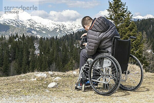 Foto eines Mannes im Rollstuhl mit Kamera in der Natur  der schöne Berge fotografiert