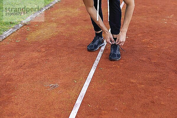 Junger Mann bindet Schuhe und bereitet sich auf das morgendliche Joggen im Freien auf der Laufstrecke vor