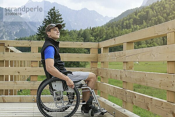 Behinderter junger Mann im Rollstuhl auf einem hölzernen Brückenpfad  der die Natur und die schöne Aussicht genießt